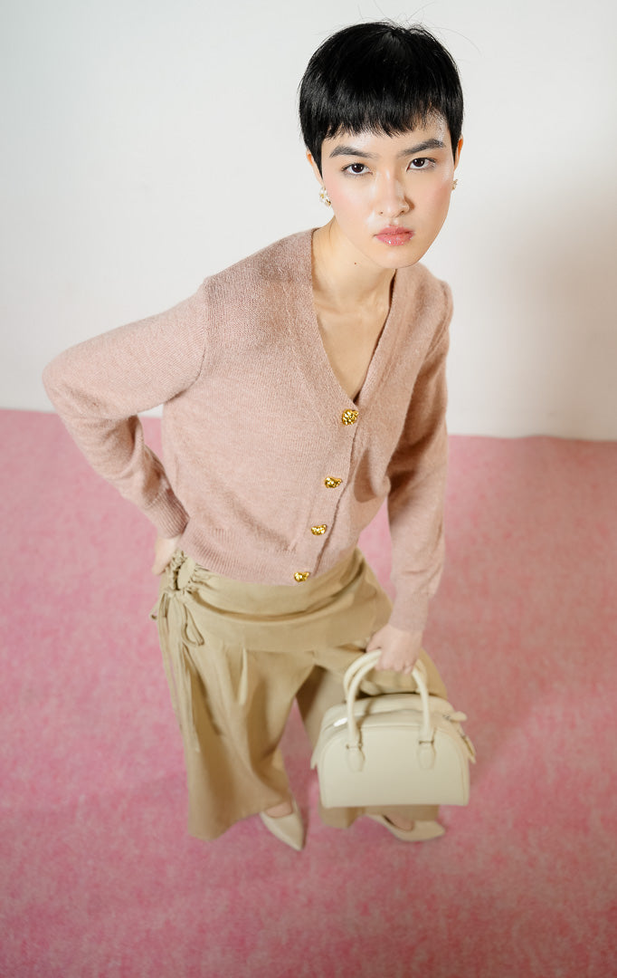 Model wanita bersandar di sofa mengenakan Yonna Cardigan warna dusty pink, atasan baju crop cardigan rajut bulu halus wanita leher V-neck dengan kancing emas mewah.