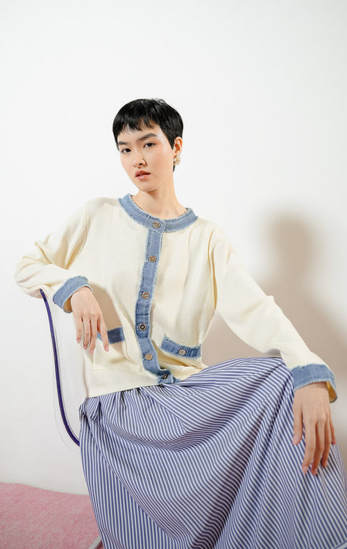Model wanita berpose duduk mengenakan Peyton Outer warna ivory, baju cardigan rajut wanita warna putih gading dengan kombinasi aksen trim bahan jeans denim biru ber-rumbai.