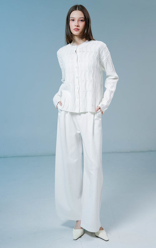 Model wanita mengenakan Twyla Textured Crew Neck Button-Up Cardigan warna white, luaran cardigan rajut wanita lengan panjang berwarna putih bersih dengan tekstur vertikal dan kancing depan.