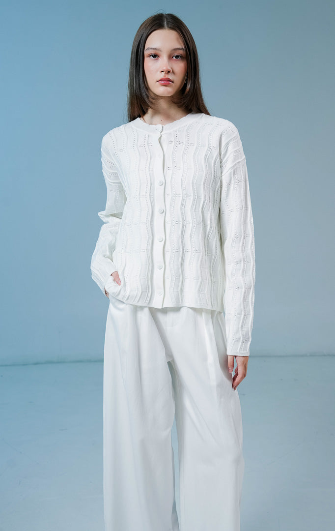 Model wanita mengenakan Twyla Textured Crew Neck Button-Up Cardigan warna white, luaran cardigan rajut wanita lengan panjang berwarna putih bersih dengan tekstur vertikal dan kancing depan.