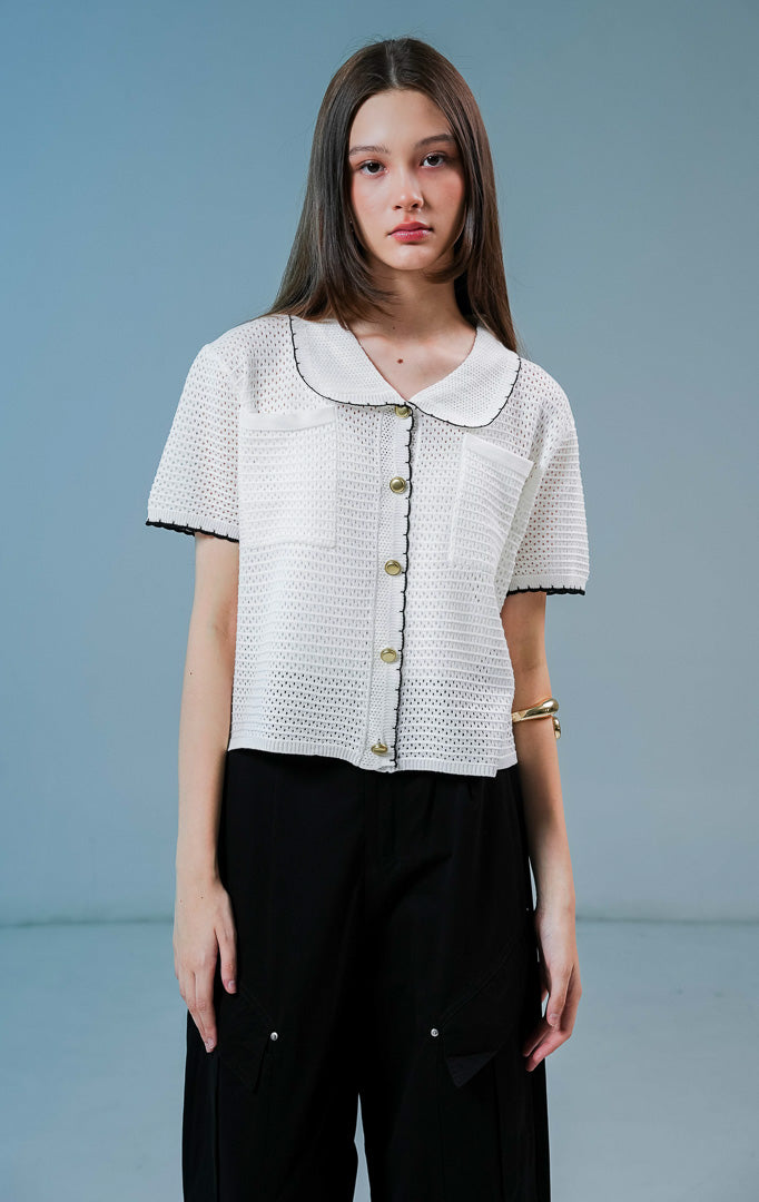Model wanita mengenakan Mylah Pockets Knit Cardigan warna white, luaran cardigan rajut wanita lengan pendek berwarna putih dengan detail kerah bulat, tepian hitam, dan kancing emas.