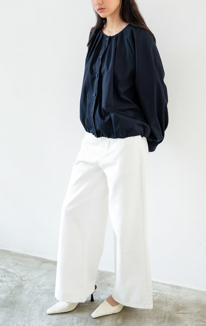Atasan wanita lengan panjang warna biru navy (navy blue) Catharine Top berbahan katun twill (cotton twill) dengan kerah bulat, bukaan kancing depan, dan detail tali serut di bagian bawah (drawstring hem).