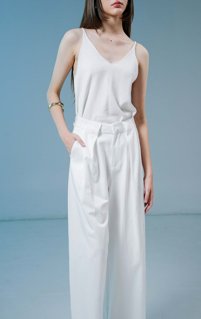 Model wanita mengenakan Normandy Pleated Straight Pants warna white, celana panjang bahan katun wanita berwarna putih dengan detail lipit depan dan potongan straight-leg.