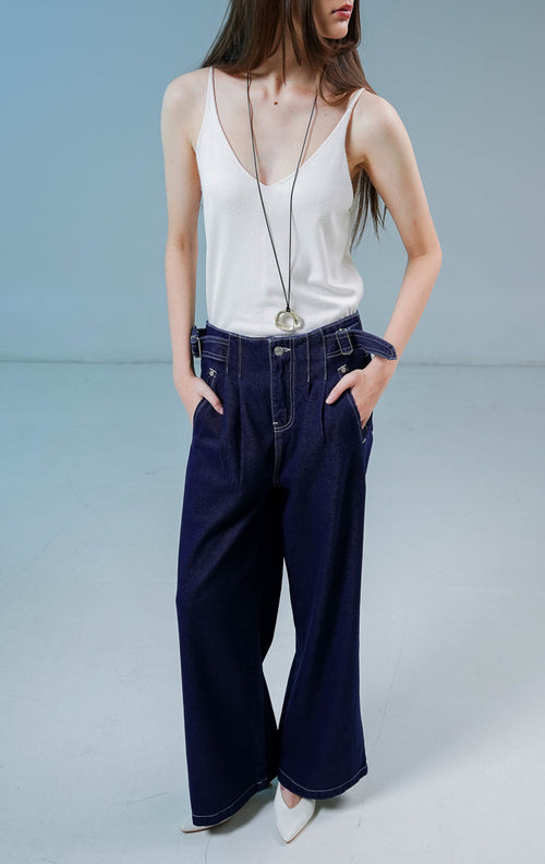 Model wanita mengenakan Luneth Pants warna dark denim, celana panjang kulot jeans wanita berpotongan longgar dengan detail lipit depan dan gesper samping unik.