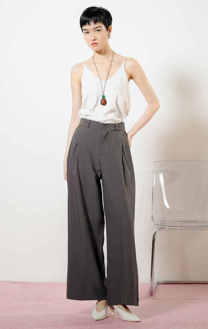 Model wanita mengenakan Earhart Inverted Pleat Wide Leg Pants warna grey, celana panjang kulot bahan poliester wanita berwarna abu-abu gelap dengan detail lipit depan dan potongan kaki lebar.