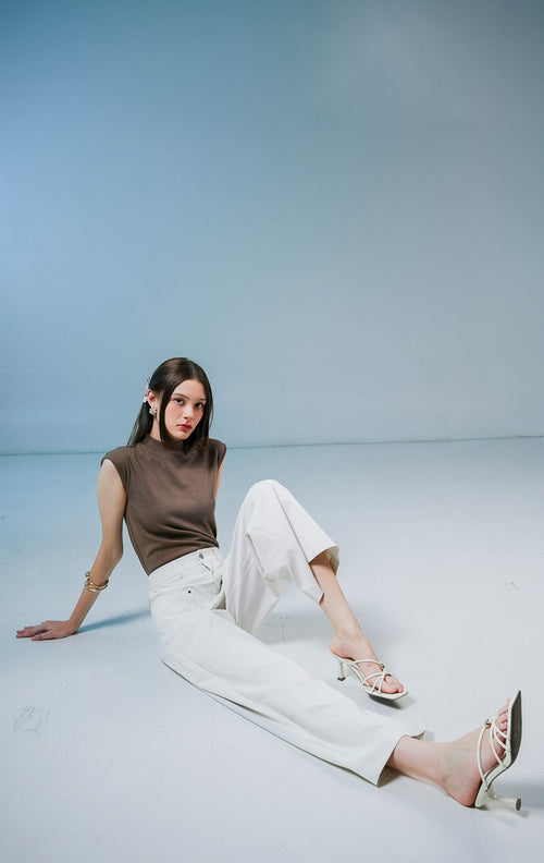 Model wanita mengenakan Eleinna Straight Leg Pants warna ivory atau putih tulang, celana panjang katun berpotongan lurus dengan detail saku depan.