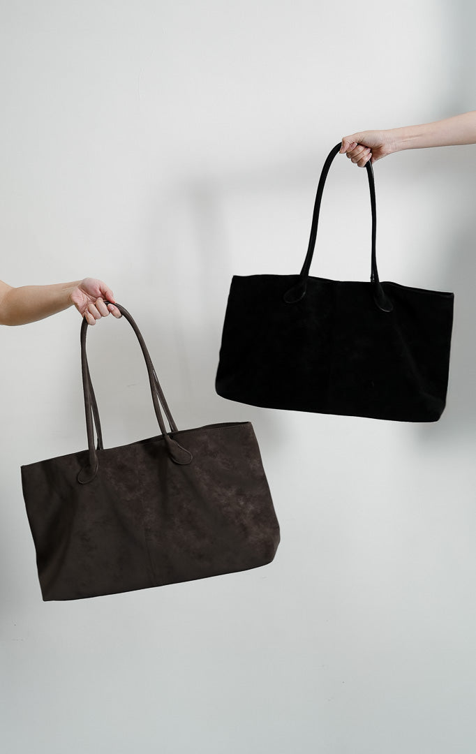 Tas tote wanita Chiro warna hitam pekat menampilkan siluet lebar terstruktur berbahan suede premium lembut dengan dua tali bahu panjang melengkung (double shoulder strap).