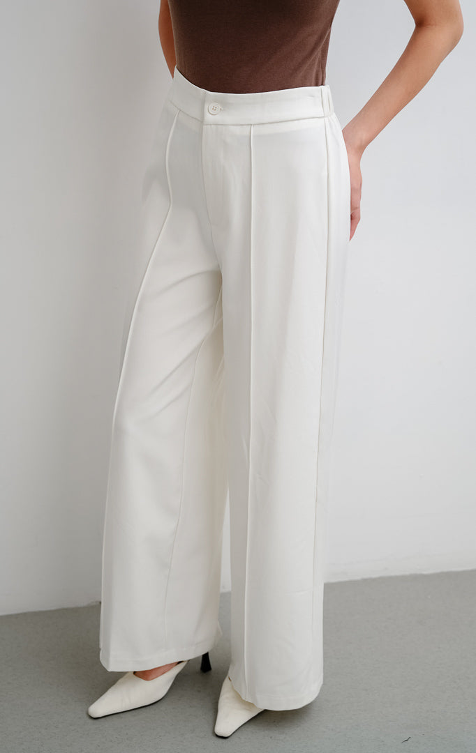 Celana panjang wanita warna putih Clarence Pants dengan potongan lurus (straight-cut), detail lipatan depan (front darts), dan pinggang karet bagian belakang.