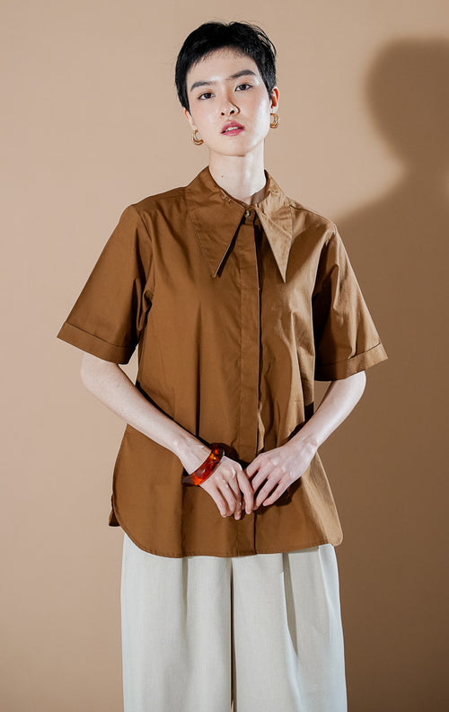 Model wanita mengenakan Cloudie Top Brown, kemeja lengan pendek berwarna cokelat dengan detail kerah lebar dan bahan katun yang berstruktur dari This Is April.