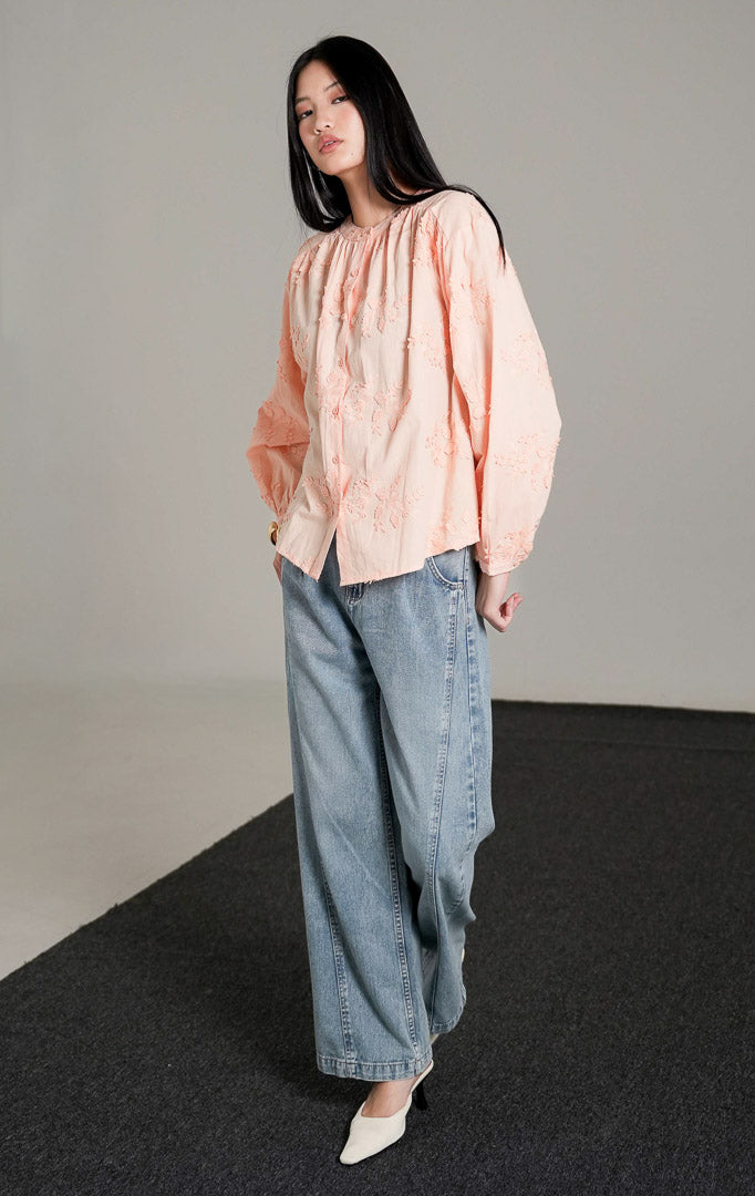 Colette Top warna peach berbahan katun dengan detail bordir bunga, kerah bulat, dan kancing depan, dipadukan dengan celana jeans longgar.