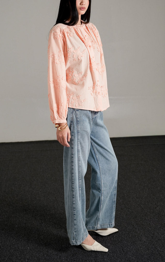 Colette Top warna peach berbahan katun dengan detail bordir bunga, kerah bulat, dan kancing depan, dipadukan dengan celana jeans longgar.