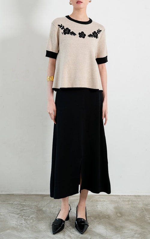 Atasan rajut wanita lengan pendek warna khaki Coreen Top berpotongan peplum dengan kerah bulat lis hitam kontras (black ribbed trim), serta aksen bordir bunga hitam di bagian dada (black floral embroidery).