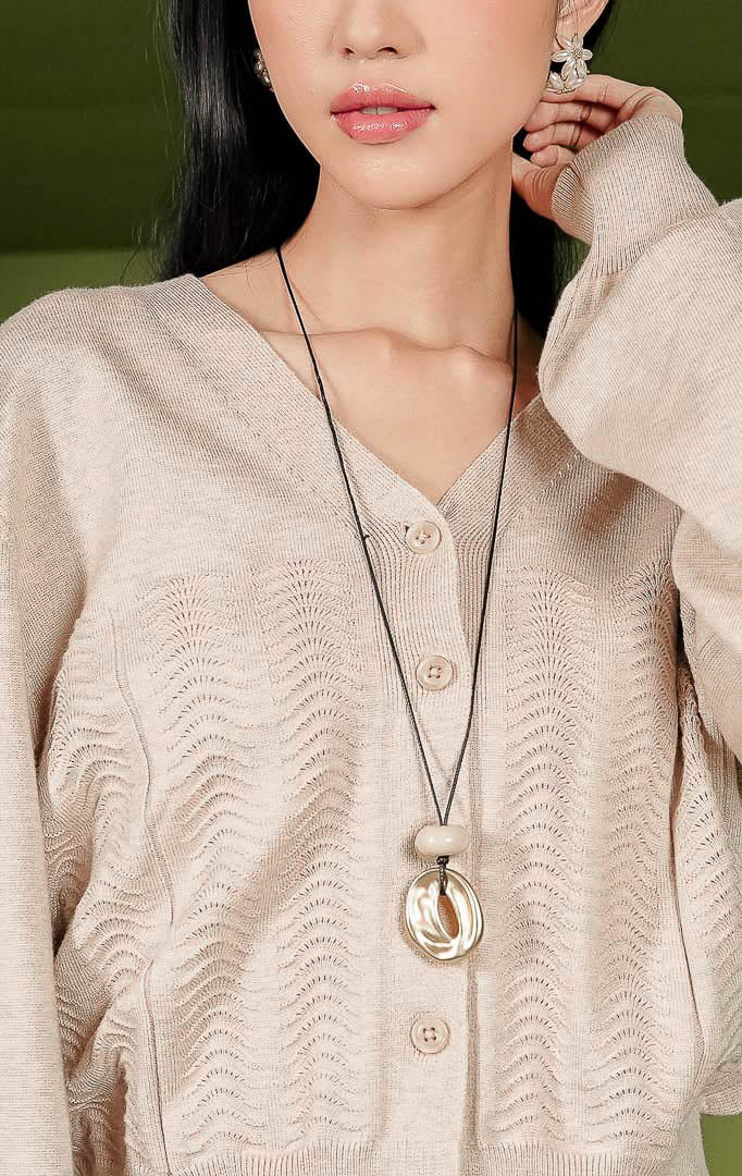 Kardigan rajut wanita Daliya Cardigan warna beige polos dengan kerah V-neck, kancing depan, dan detail tekstur rajutan bermotif gelombang pada area depan bawah.