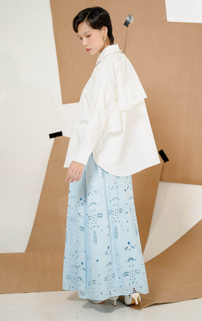 Model tampak samping mengenakan Dayle Top White, produk kemeja kerja kantor wanita lengan panjang warna putih dengan detail ruffle di punggung dipadukan rok panjang biru.