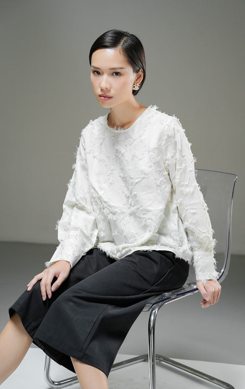 Blouse wanita Demetrius Top warna ivory krem muda lengan panjang dengan tekstur bulu halus (fringe jacquard), kerah bulat, dan kancing belakang.