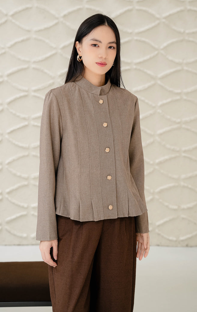 Outerwear wanita tanpa kerah (round-neck) Denali warna brown (cokelat) bertekstur lipit vertikal (pleated) dengan detail kancing emas (gold buttons) tampak depan.