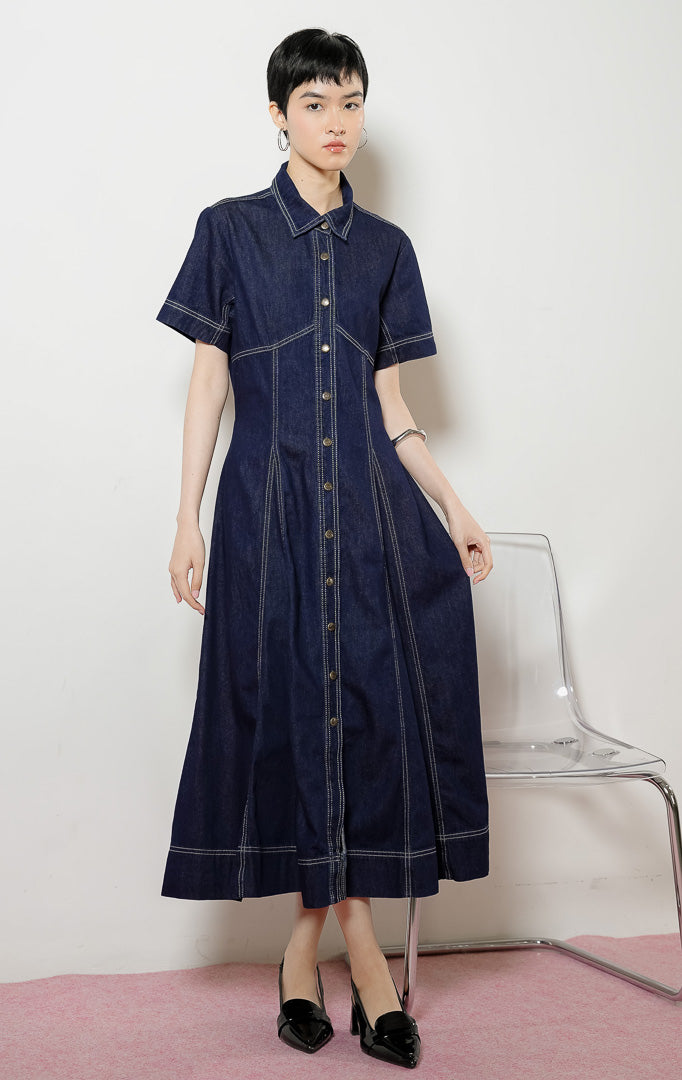 Model wanita mengenakan Lumera Classic Flared Maxi Dress warna dark denim, gaun dress panjang bahan jeans wanita lengan pendek berwarna biru dongker dengan detail jahitan kontras putih.