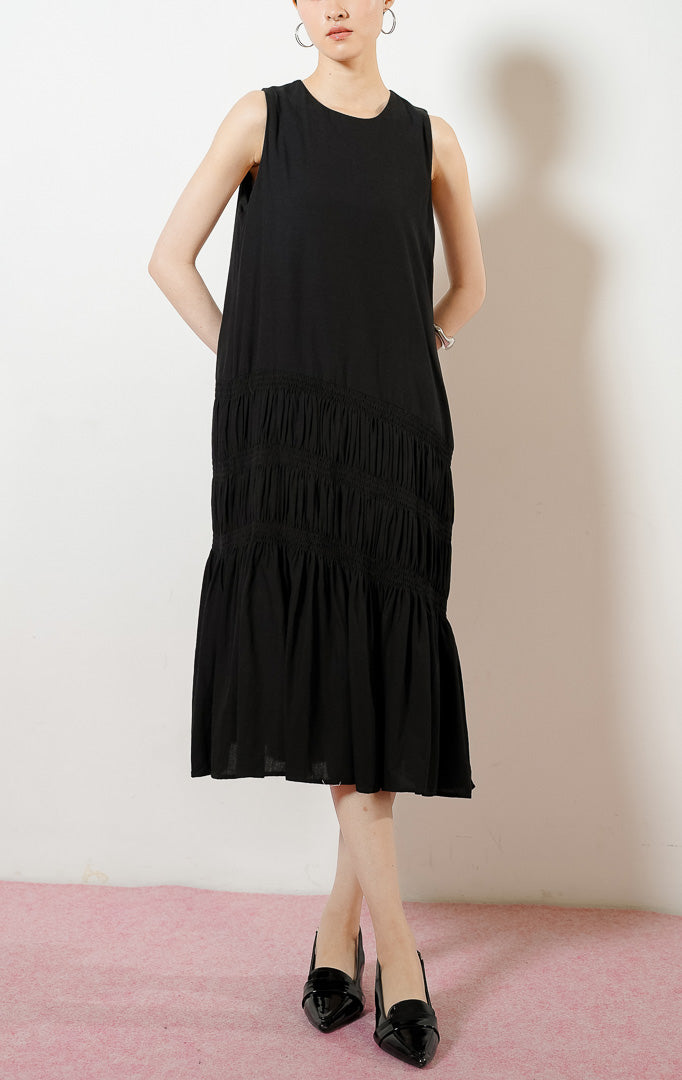 Model wanita mengenakan Ravena Shirred Bodice Drop-Tier Maxi Dress warna black, gaun panjang dress tanpa lengan wanita warna hitam dengan detail aksen serut karet smok bertingkat di rok.