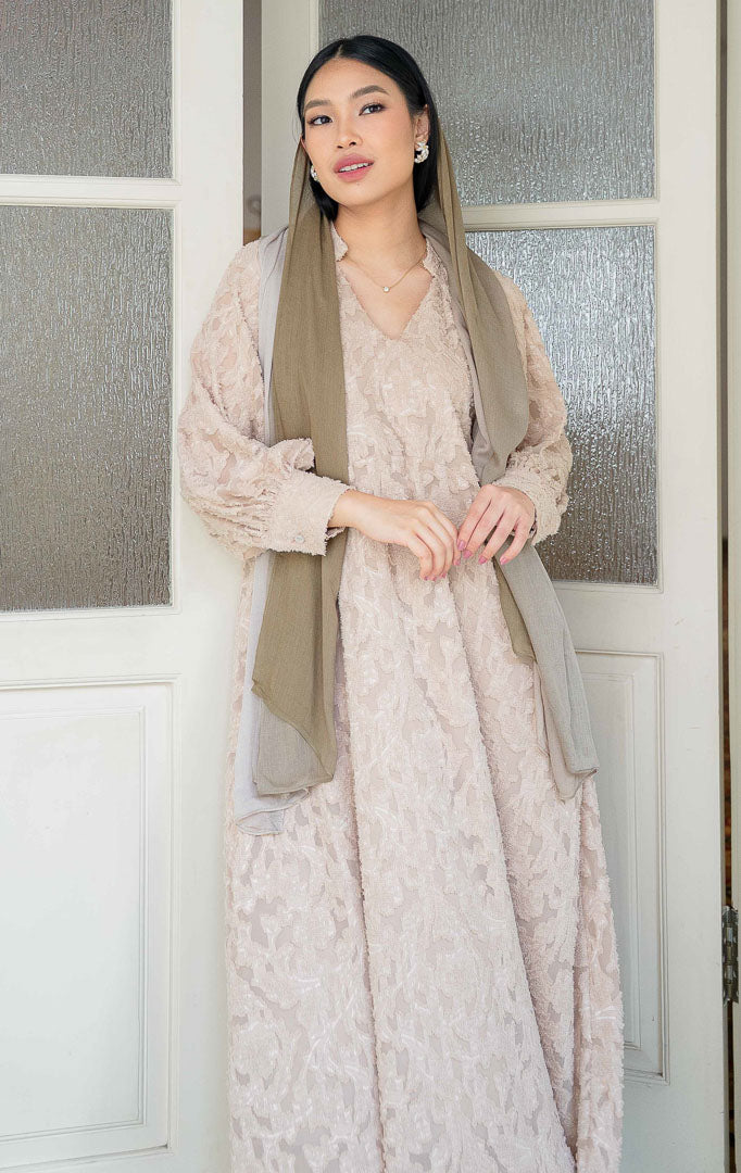 Model wanita mengenakan EID Aisya Dress Brown, dress pesta panjang
bahan floral jacquard organza bertekstur dengan kerah V neck dan lengan
panjang transparan yang elegan.