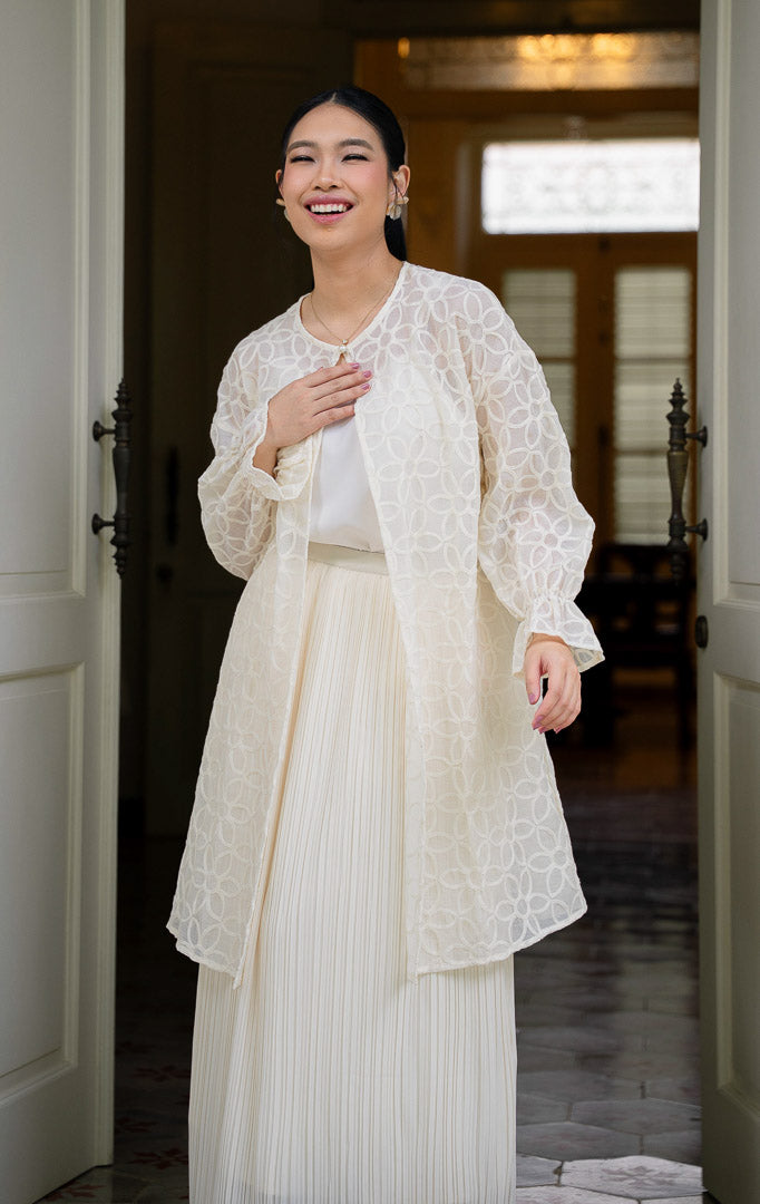 EID Fariha Top Ivory, atasan wanita warna putih gading bahan cotton voile
transparan dengan motif bordir bunga lingkaran penuh, kancing tunggal di
leher, dan ujung lengan model flare kerut.