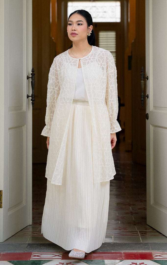 EID Fariha Top Ivory, atasan wanita warna putih gading bahan cotton voile
transparan dengan motif bordir bunga lingkaran penuh, kancing tunggal di
leher, dan ujung lengan model flare kerut.