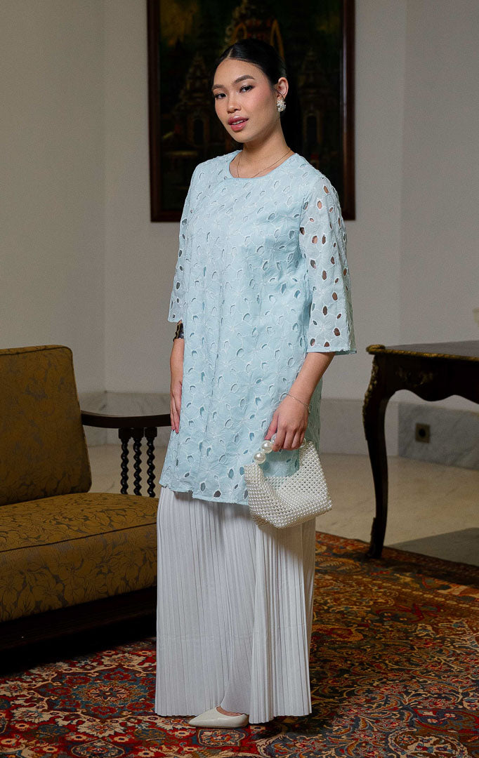 EID Latifa Top Blue, atasan wanita warna biru muda bahan katun dengan
motif bordir eyelet berlubang dan detail kancing mutiara miring asimetris di
bagian depan.