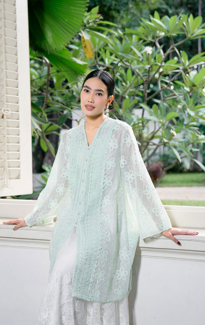 EID Naseha Top Sage, atasan blouse wanita warna hijau sage bahan cotton
voile transparan dengan motif bordir bunga dan detail panel renda lace
vertikal lebar di depan.