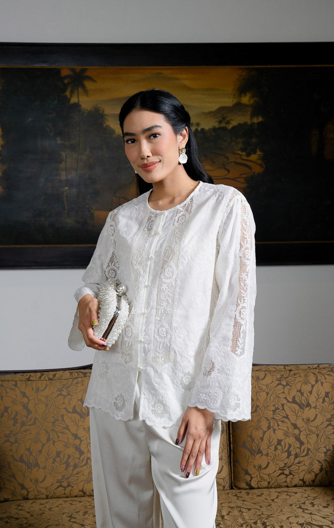 EID Qonita Top White, atasan blouse wanita warna putih bahan lace bordir
floral dengan potongan pendek modern, kancing depan, dan detail panel
renda vertikal.