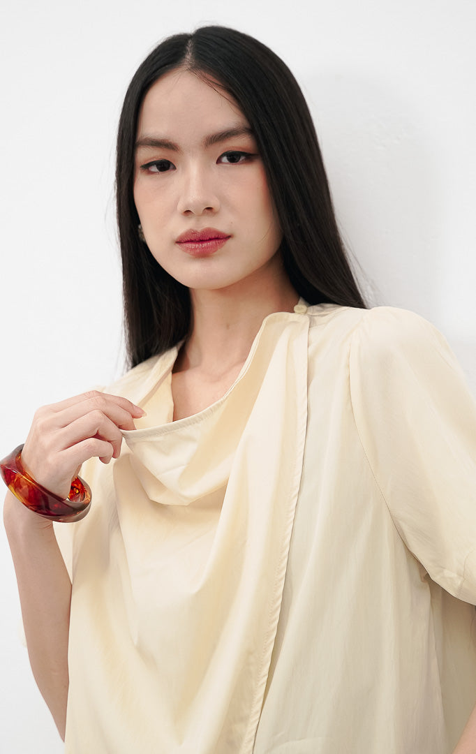 Close up model mengenakan Eileen Top warna yellow, menampilkan detail kerah draped cowl neck yang elegan dan kancing dekoratif di bahu.