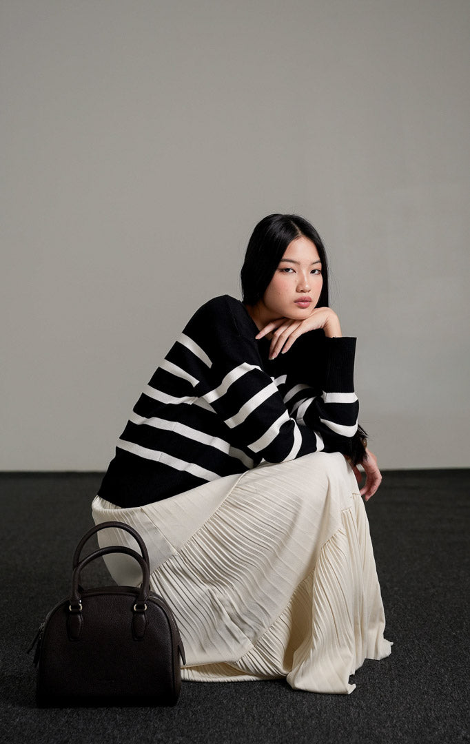 Elbie Striped Knit Sweater lengan panjang warna hitam dengan motif garis horizontal putih, dipadukan dengan rok panjang lipit warna krem dan sepatu mules hitam.
