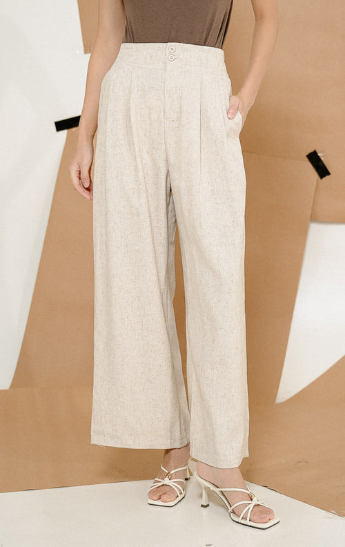 Model berdiri mengenakan Elona Chic Double Button Pants Ivory, produk celana panjang wanita dengan potongan high waist longgar warna krem ivory dipadukan atasan cokelat.