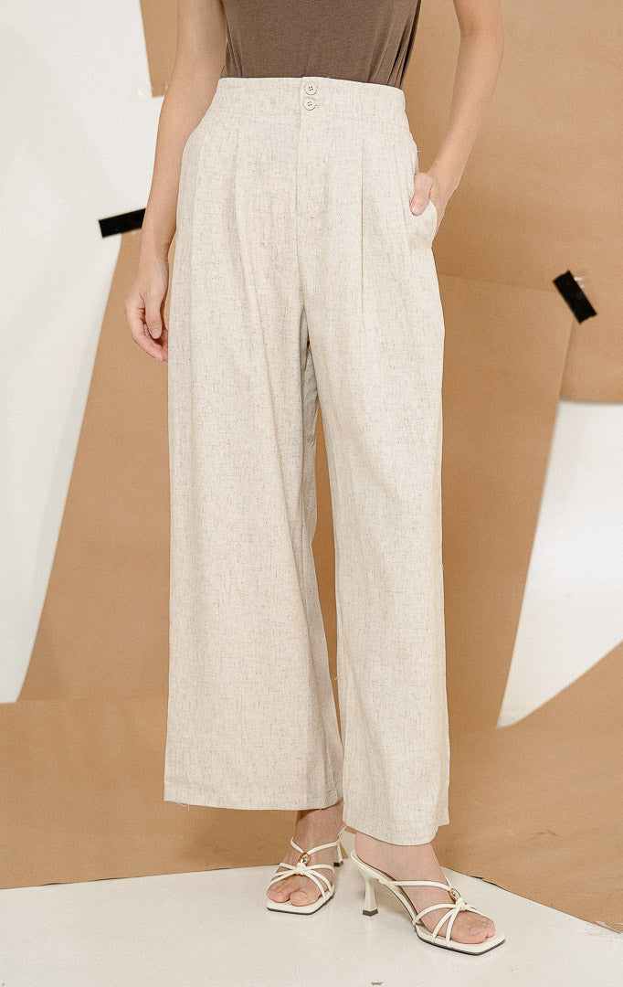 Model berdiri mengenakan Elona Chic Double Button Pants Ivory, produk celana panjang wanita dengan potongan high waist longgar warna krem ivory dipadukan atasan cokelat.