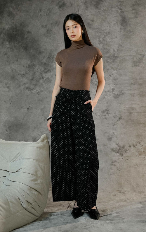 Celana panjang wanita Evelyna warna hitam bermotif polkadot dengan cutting barrel pants, berbahan denim, dilengkapi karet pinggang belakang dan aksen tali pita.