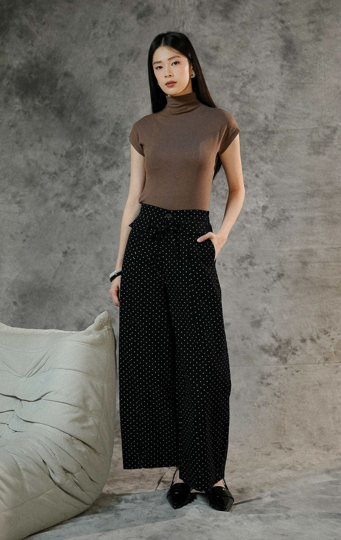 Celana panjang wanita Evelyna warna hitam bermotif polkadot dengan cutting barrel pants, berbahan denim, dilengkapi karet pinggang belakang dan aksen tali pita.
