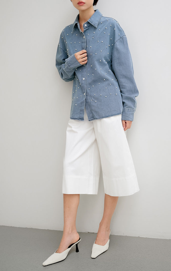 Atasan kemeja denim wanita lengan panjang Faye Top dengan detail hiasan mutiara (pearl details), bukaan kancing depan, dan siluet berstruktur.