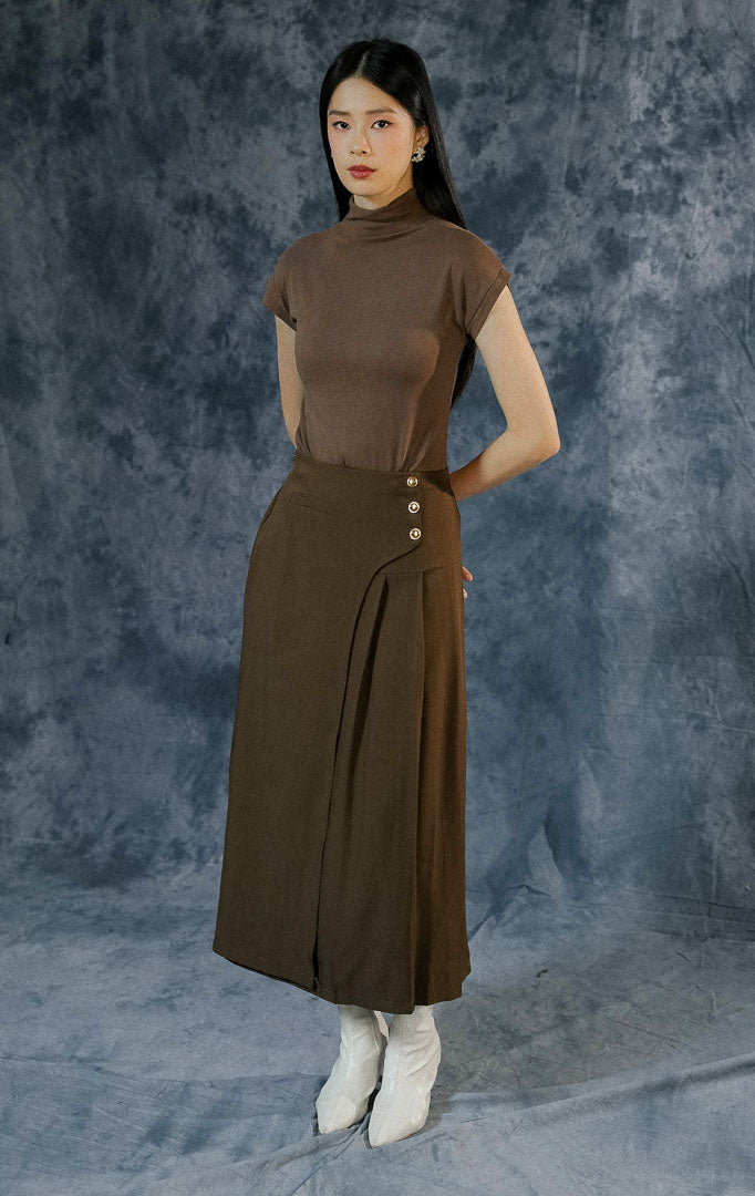 Rok panjang wanita Florida warna dark brown dengan cutting wrap front, detail lipit (pleat), dekorasi kancing emas, serta karet pinggang belakang.