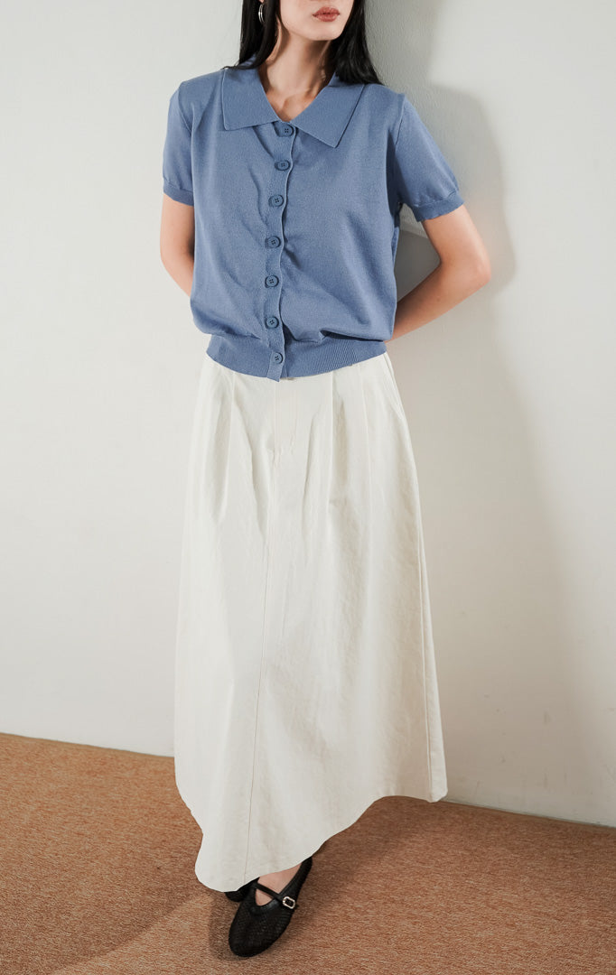 Gabriela Top Dusty Blue, atasan rajut lengan pendek berkerah warna biru dusty dengan kancing depan, dipadukan dengan rok panjang putih.