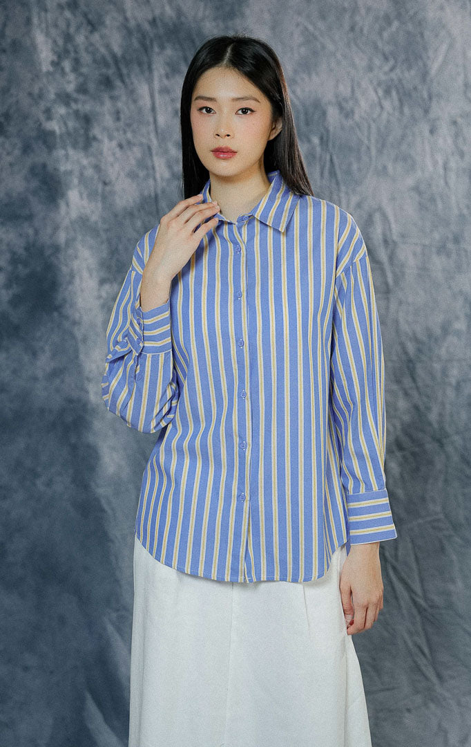 Atasan kemeja lengan panjang wanita Giselda warna biru klasik dengan motif garis-garis kuning, dilengkapi kerah rapi dan kancing depan penuh.