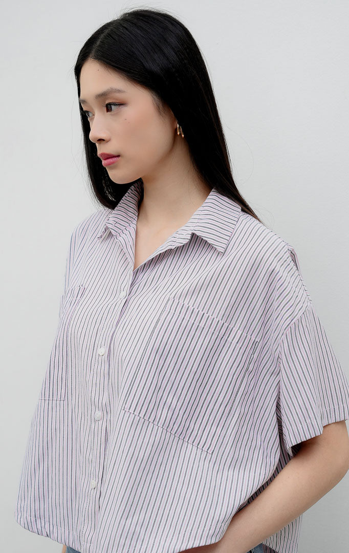 Kemeja katun wanita lengan pendek potongan boxy warna merah muda (pink) Hampton Top berkerah (spread collar) dengan motif garis vertikal (striped pattern), kancing depan, dan saku dada.