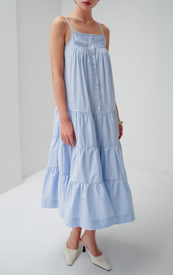 Maxi dress panjang wanita warna biru muda (light blue) Hathaway Dress berbahan katun dengan detail smocked yoke di dada, tali spageti (adjustable straps), dan gaun berundak (tiered silhouette).