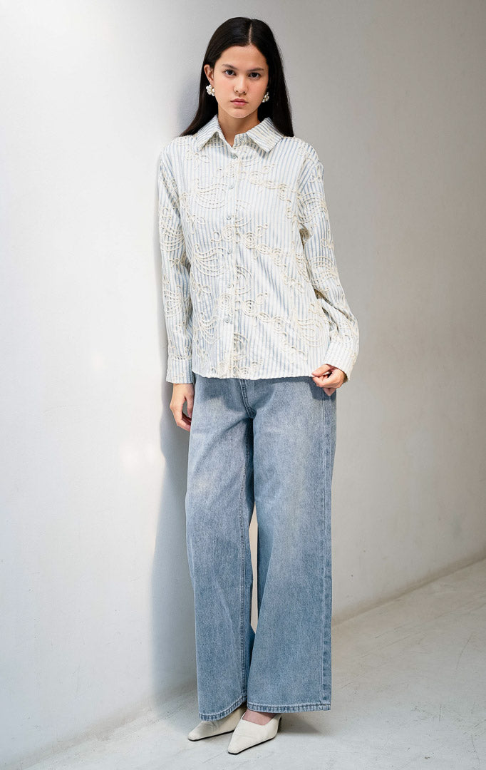 Kemeja wanita lengan panjang warna biru (blue) Hawthorne Top berbahan tekstur motif garis dengan detail bordir timbul abstrak (intricate looped embroidery), kerah lebar (oversized collar), bukaan kancing depan, dan kelim melengkung (curved hem).