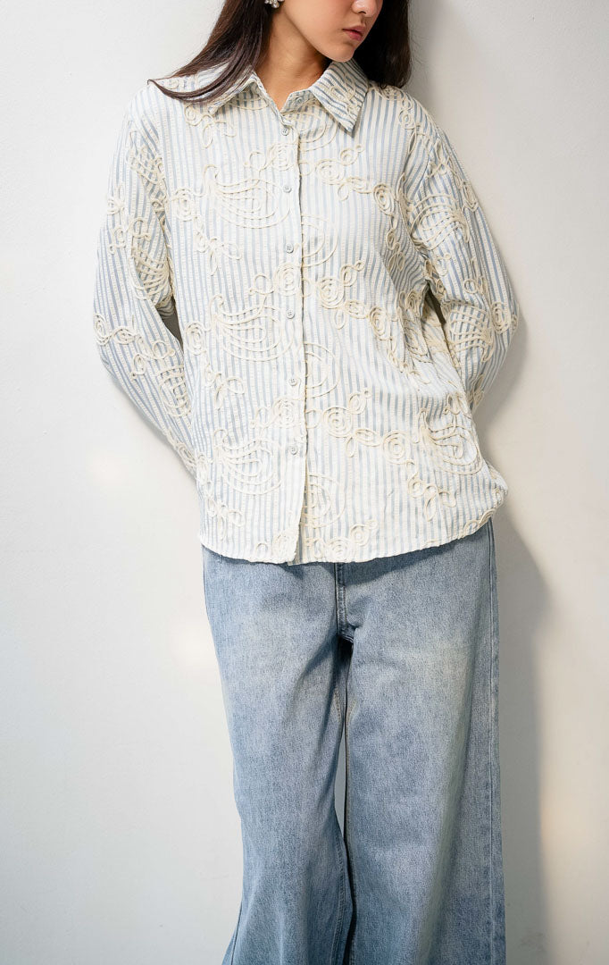 Kemeja wanita lengan panjang warna biru (blue) Hawthorne Top berbahan tekstur motif garis dengan detail bordir timbul abstrak (intricate looped embroidery), kerah lebar (oversized collar), bukaan kancing depan, dan kelim melengkung (curved hem).