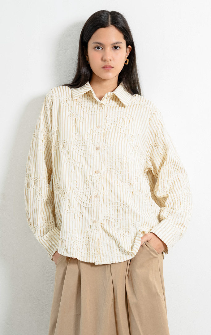Kemeja wanita lengan panjang warna khaki Hawthorne Top berbahan tekstur motif garis dengan detail bordir timbul abstrak (intricate looped embroidery), kerah lebar (oversized collar), bukaan kancing depan, dan kelim melengkung (curved hem).