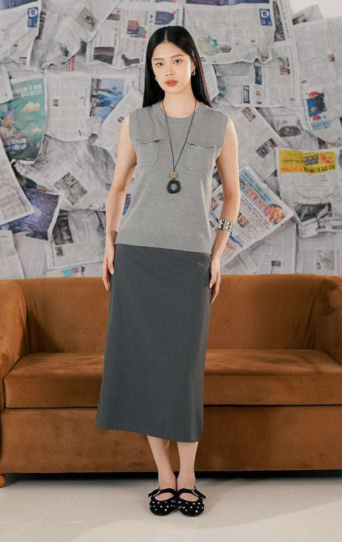 Model wanita memakai Heidi Top Grey, atasan rajut tanpa lengan (sleeveless knit top) warna abu-abu dengan kerah bulat dan detail dua saku depan, bergaya minimalis.