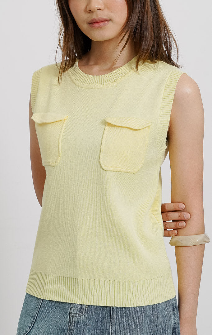 Model wanita mengenakan Heidi Top Yellow, atasan rompi rajut tanpa lengan warna kuning pastel dengan dua saku dada, dipadukan dengan rok denim panjang.
