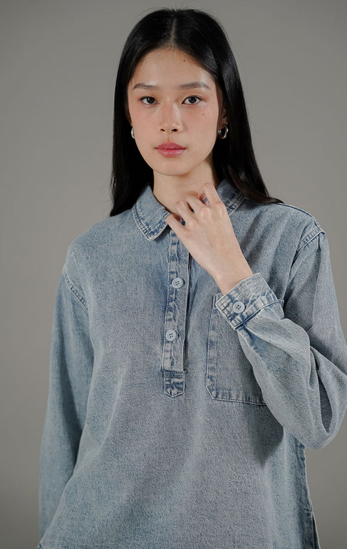 Atasan kemeja Elyse Top Denim wanita warna biru muda dari This Is April, dilengkapi kerah, kancing depan aktif parsial, dan saku dada fungsional.