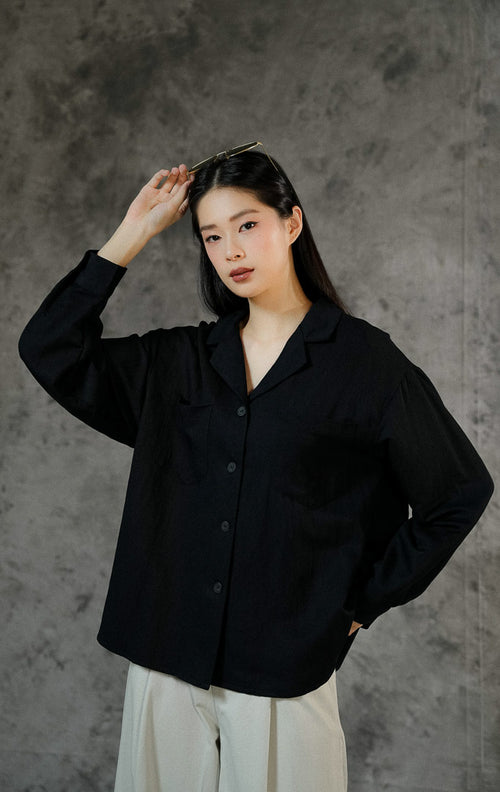 Atasan kemeja lengan panjang wanita Howard warna hitam polos dengan potongan kerah v-neck, kancing depan, dan dua saku aktif di bagian dada.
