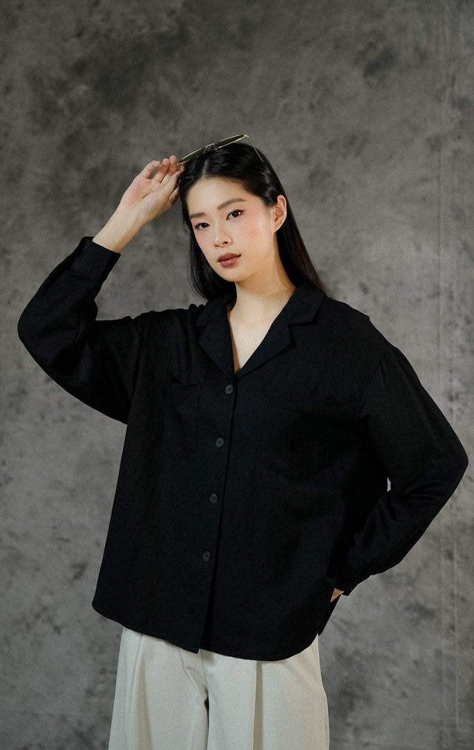 Atasan kemeja lengan panjang wanita Howard warna hitam polos dengan potongan kerah v-neck, kancing depan, dan dua saku aktif di bagian dada.