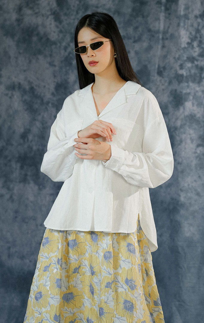 Kemeja katun wanita Howard warna putih polos dengan detail kerah v-neck modern, dua saku fungsional di depan, dan pergelangan tangan berkancing.