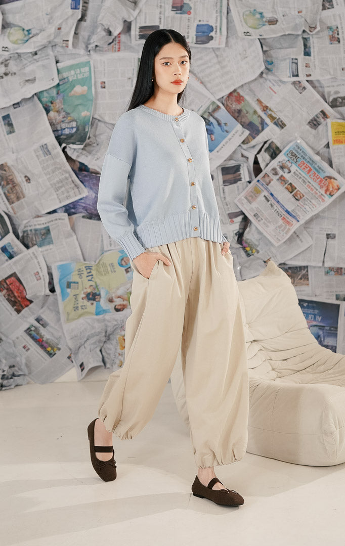 Model wanita mengenakan Hudson Cardigan Blue, sebuah cardigan rajut (knitwear) lengan panjang warna biru muda pastel dengan kerah bulat dan detail kancing depan berwarna emas.